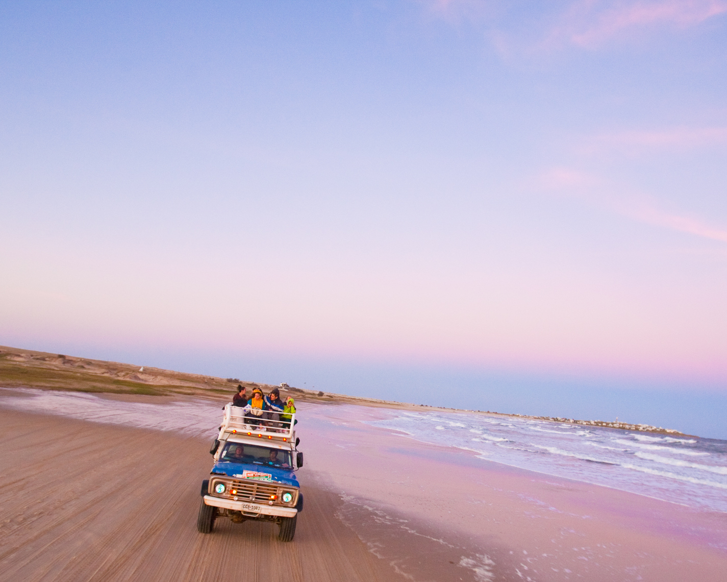 People enjoying ride in off-road vehicle on sandy beach at dusk