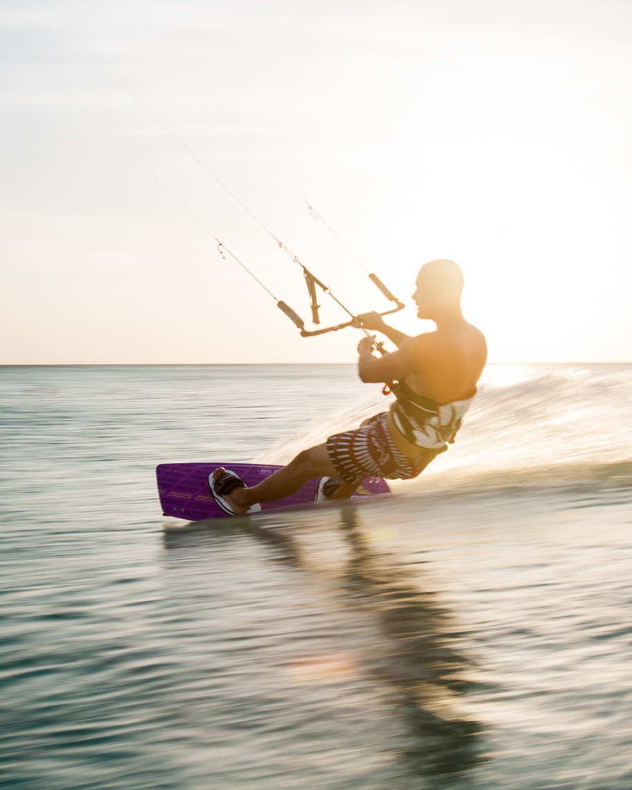 Person kitesurfing at sunset