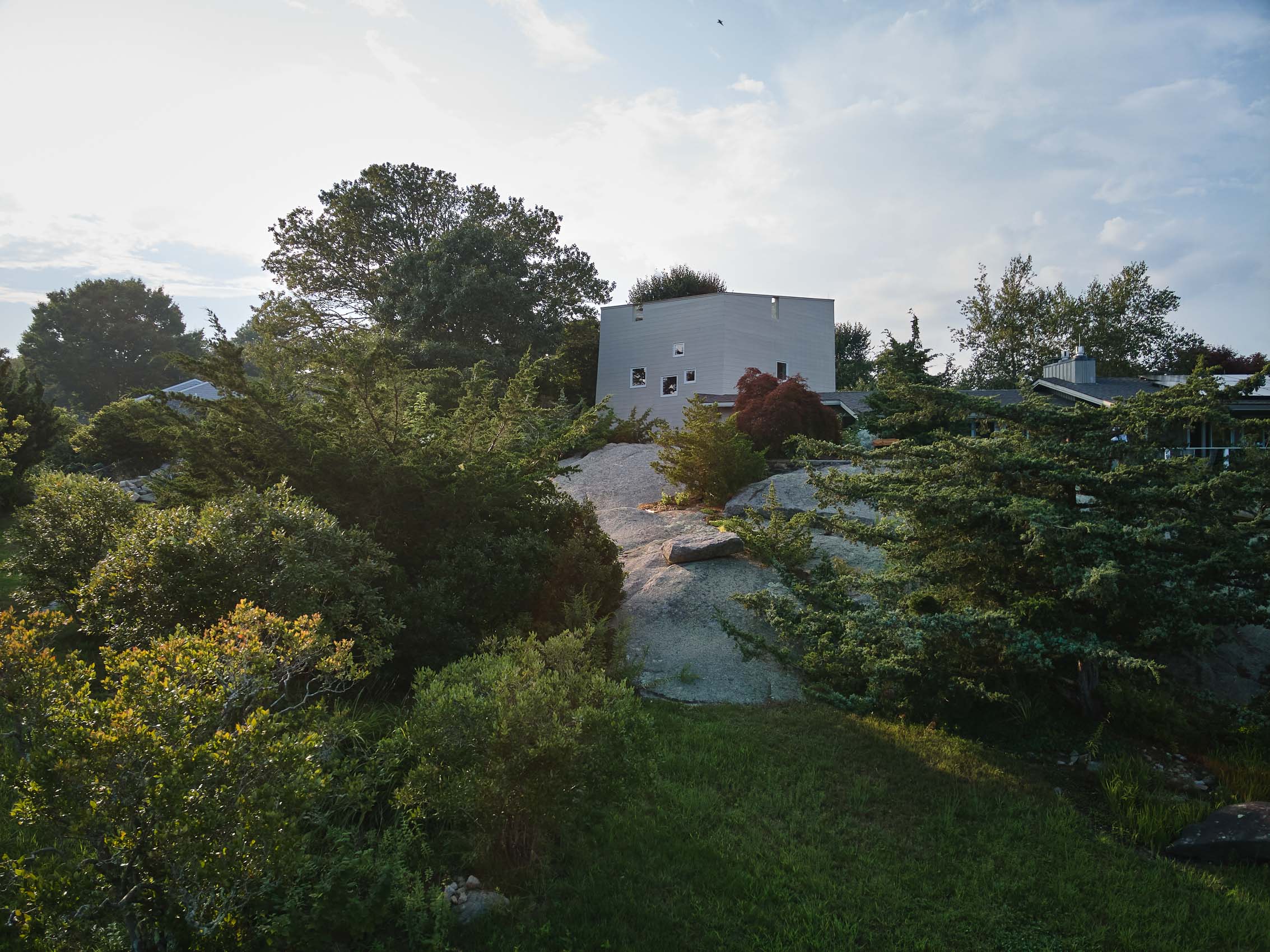 Late afternoon photograph of exterior of modern house set in  rocky terrain and trees