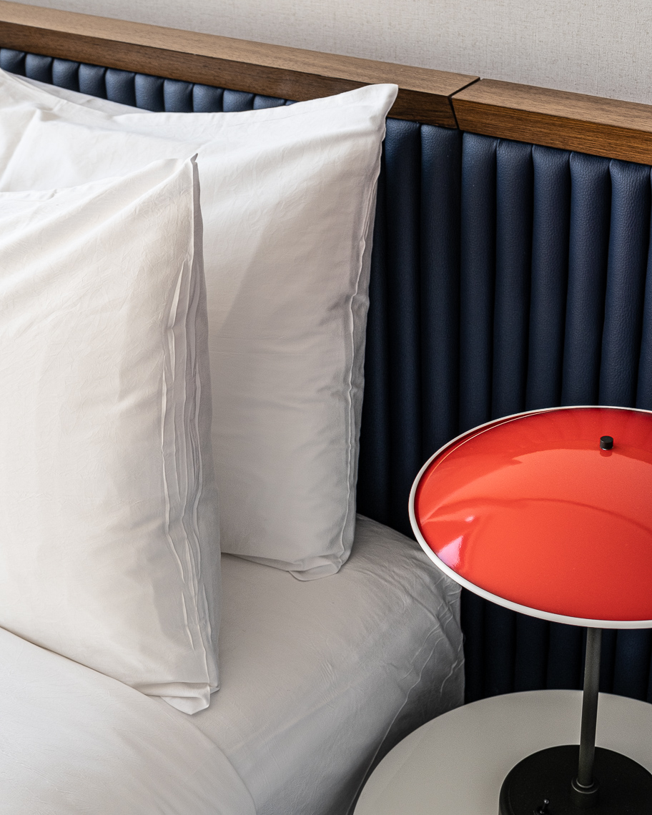 Detail of hotel bed and pillows with red bedside reading lamp